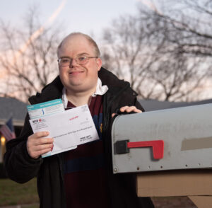 A man holding an envelope next to a mailbox.